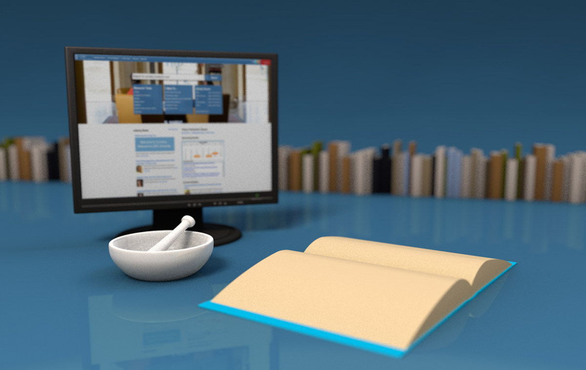 a computer monitor, a pestle, and an open book sit on the top of a table